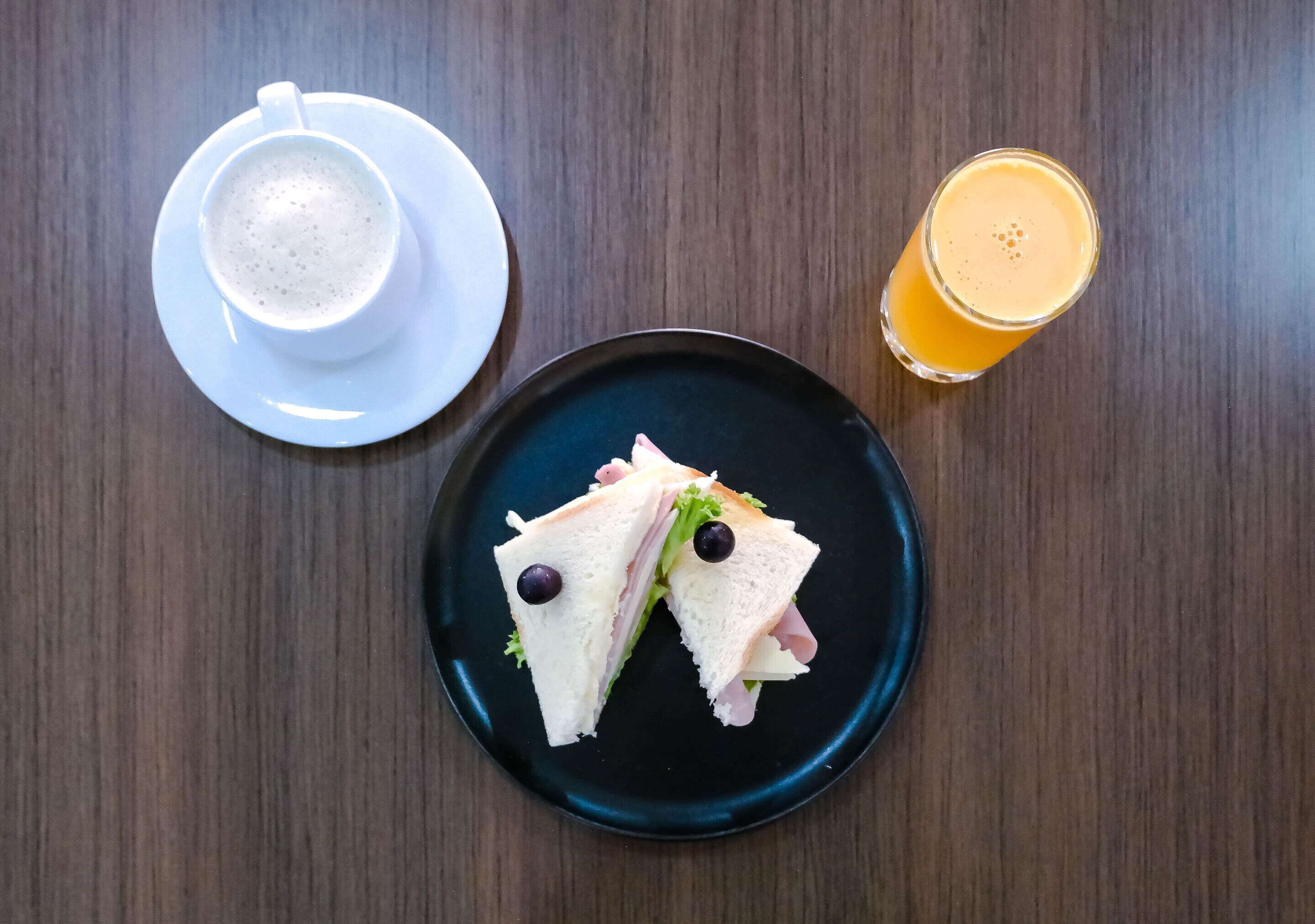 A sandwich on a plate, a cup of coffee, and a glass of orange juice on a wooden table.