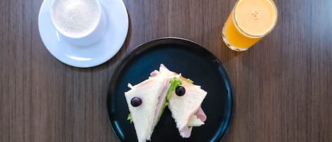 A sandwich on a plate, a cup of coffee, and a glass of orange juice on a wooden table.