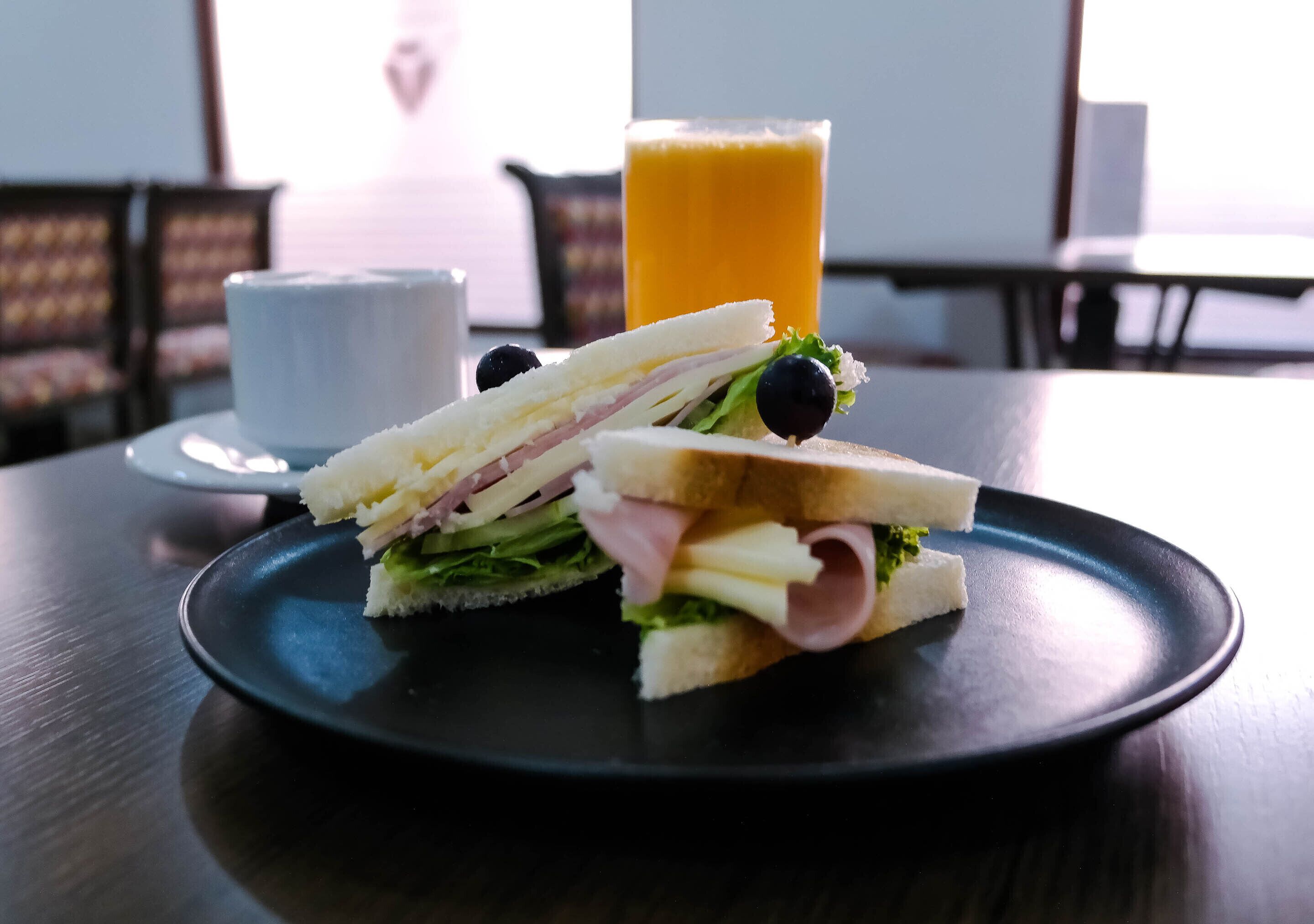 A sandwich on a black plate with a glass of orange juice in the background.
