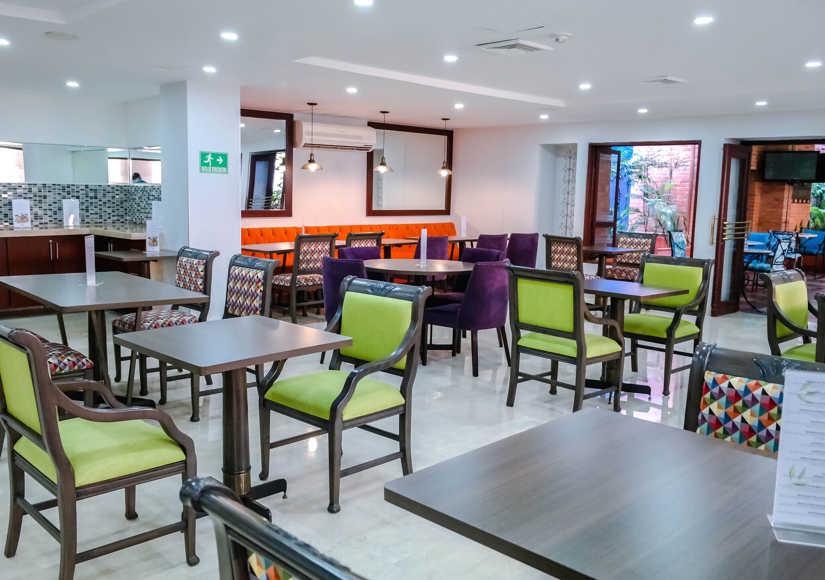 A modern restaurant with green and purple chairs, wooden tables, and a bright orange booth area.
