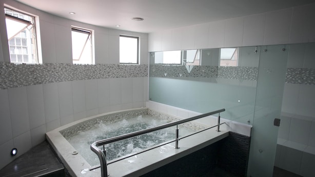 Ein modernes Badezimmer mit einer gläsernen Duschkabine, einer großzügigen Badewanne mit Glastrennwand und einer mit Mosaikmuster versehenen Wand.