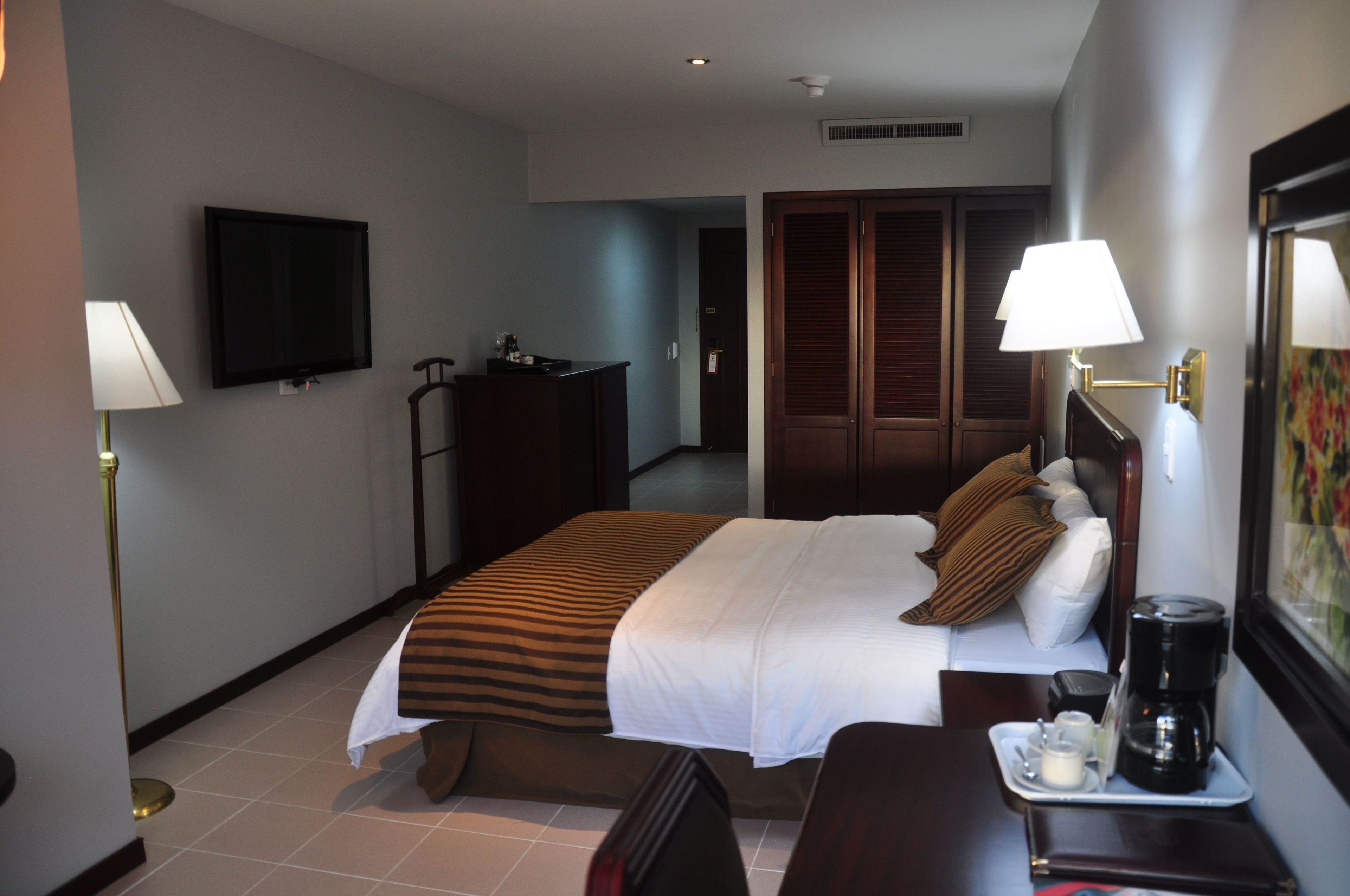 A hotel room with a bed, bedside table, lamp, TV, wardrobe, and a coffee maker.