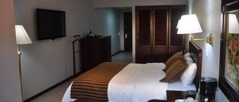 A hotel room with a bed, bedside table, lamp, TV, wardrobe, and a coffee maker.