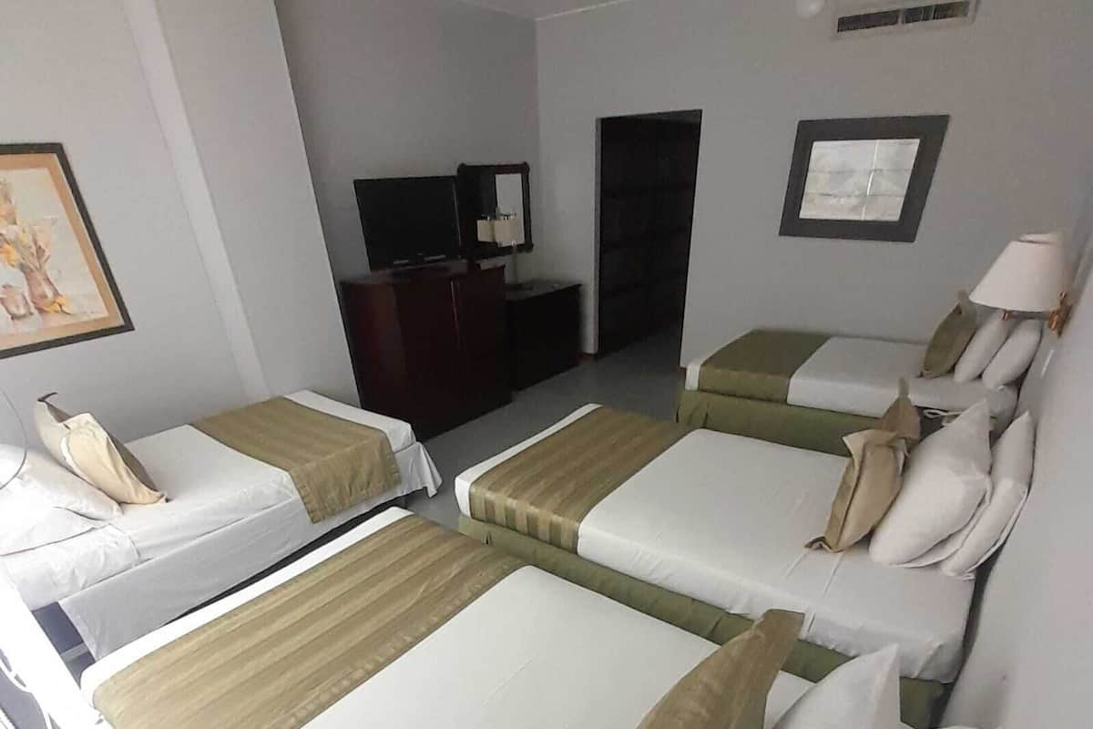 Quarto de hotel com duas camas de solteiro, uma escrivaninha com cadeira, televisão e um quadro na parede.