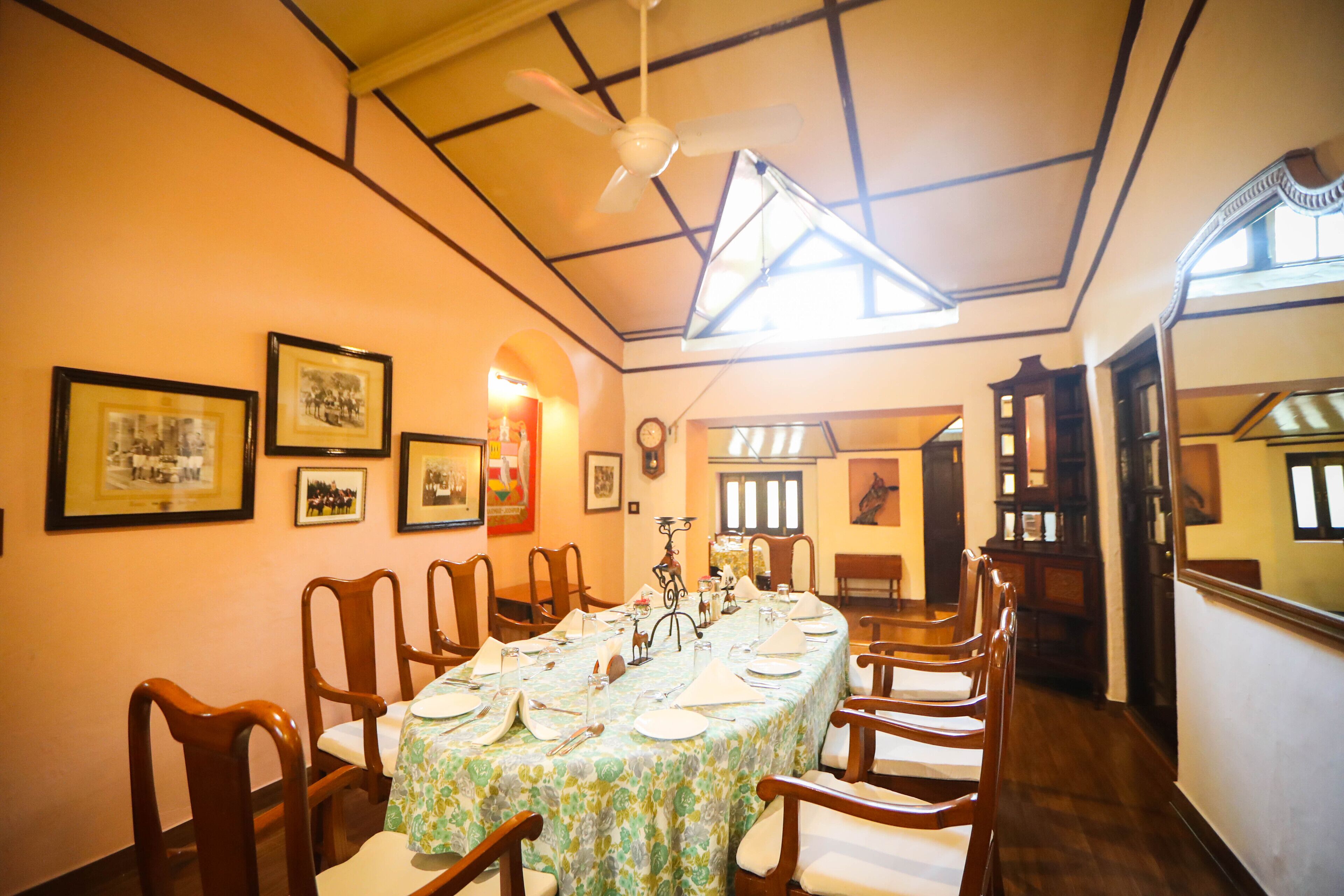 A dining area with a long table set for a meal, wooden chairs, framed pictures on the walls, and a ceiling fan.