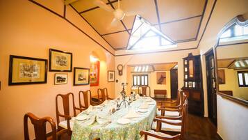 A dining area with a long table set for a meal, wooden chairs, framed pictures on the walls, and a ceiling fan.