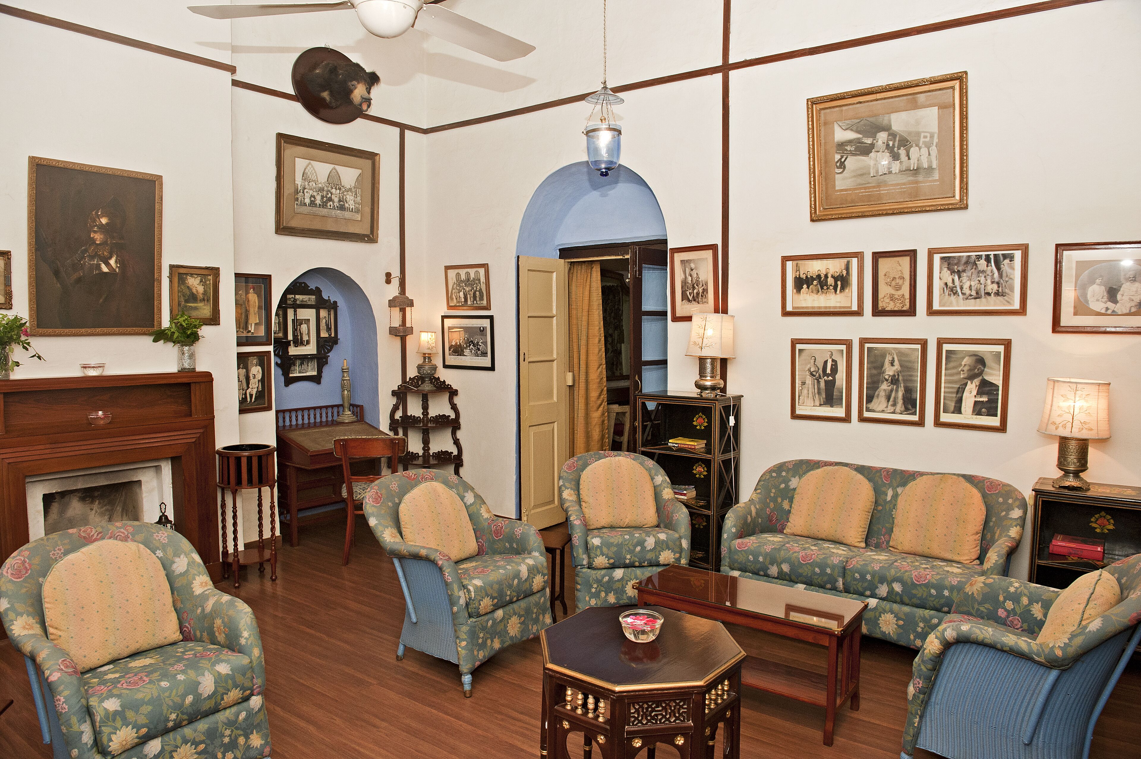A traditional living room with a fireplace, two armchairs, a sofa, a coffee table, and various framed photographs on the walls.