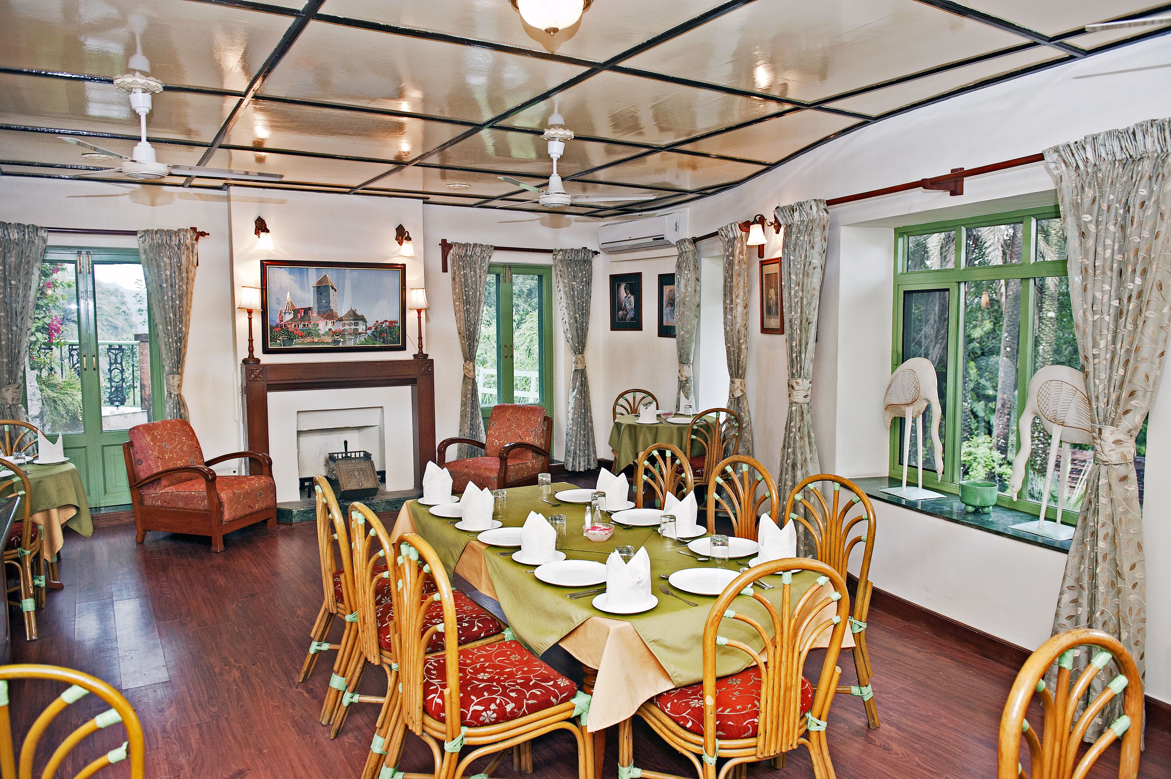 A dining area with a long table set for a meal, surrounded by wooden chairs with red cushions, a fireplace, and a painting on the wall.