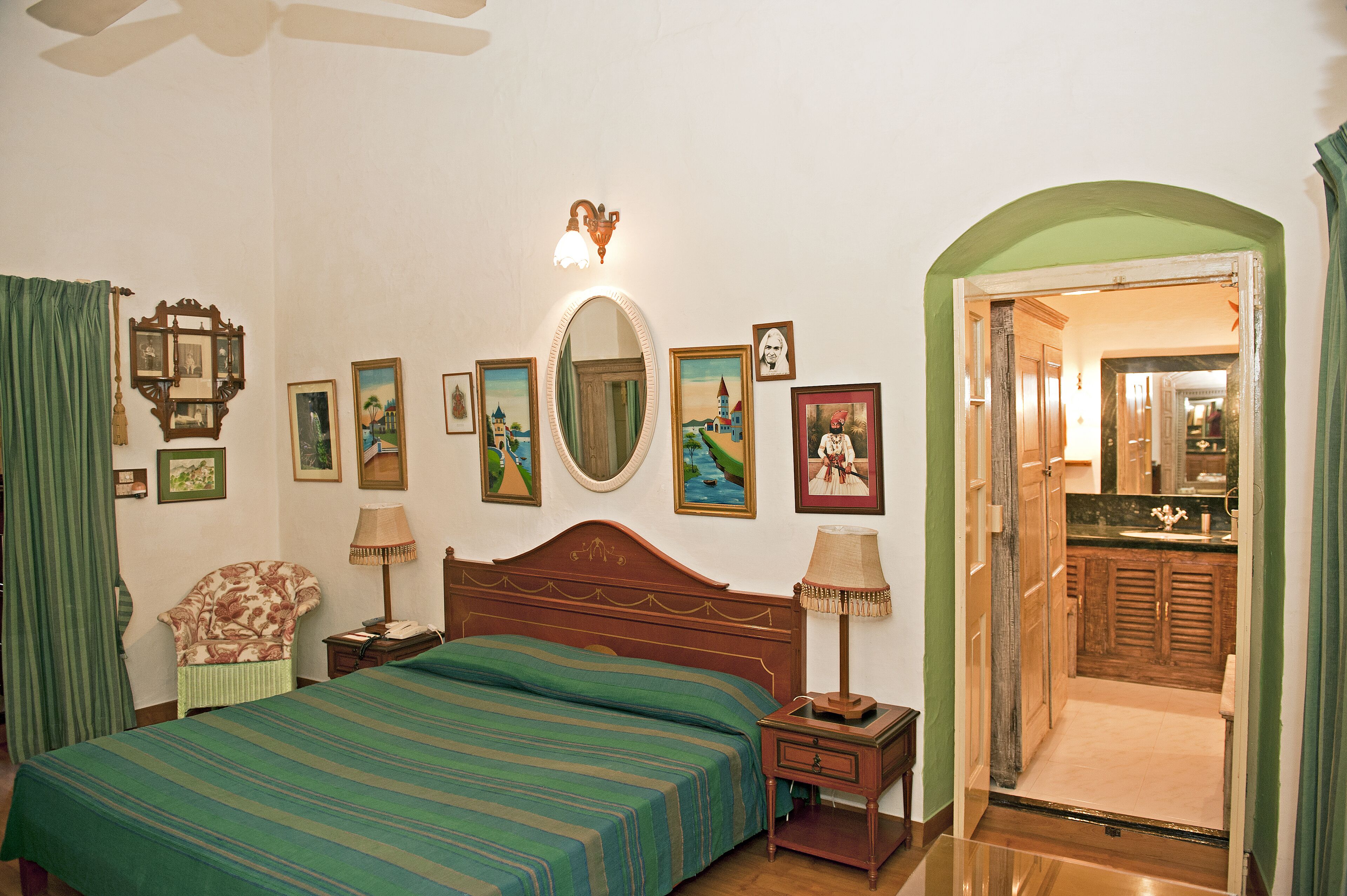 Une chambre d’hôtel comprenant un lit, une chaise, une table de chevet, un miroir et une porte donnant sur une salle de bain.