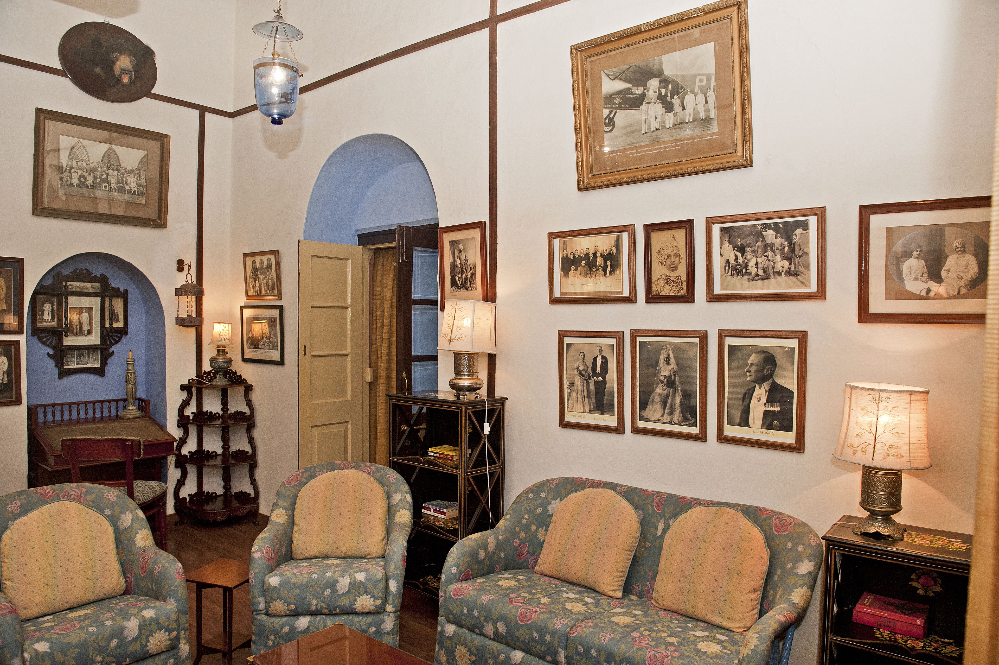 A room with two floral-patterned armchairs, a wooden side table, a lamp, and a bookshelf.