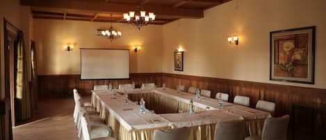 Ein Konferenzraum mit langem Tisch, Stühlen, einer Projektionsleinwand und Wandleuchten.