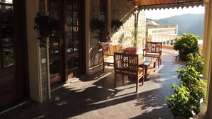 A covered patio with a stone wall, wooden doors, and potted plants. - WelcomHeritage Windsor Lodge (Ranikhet)