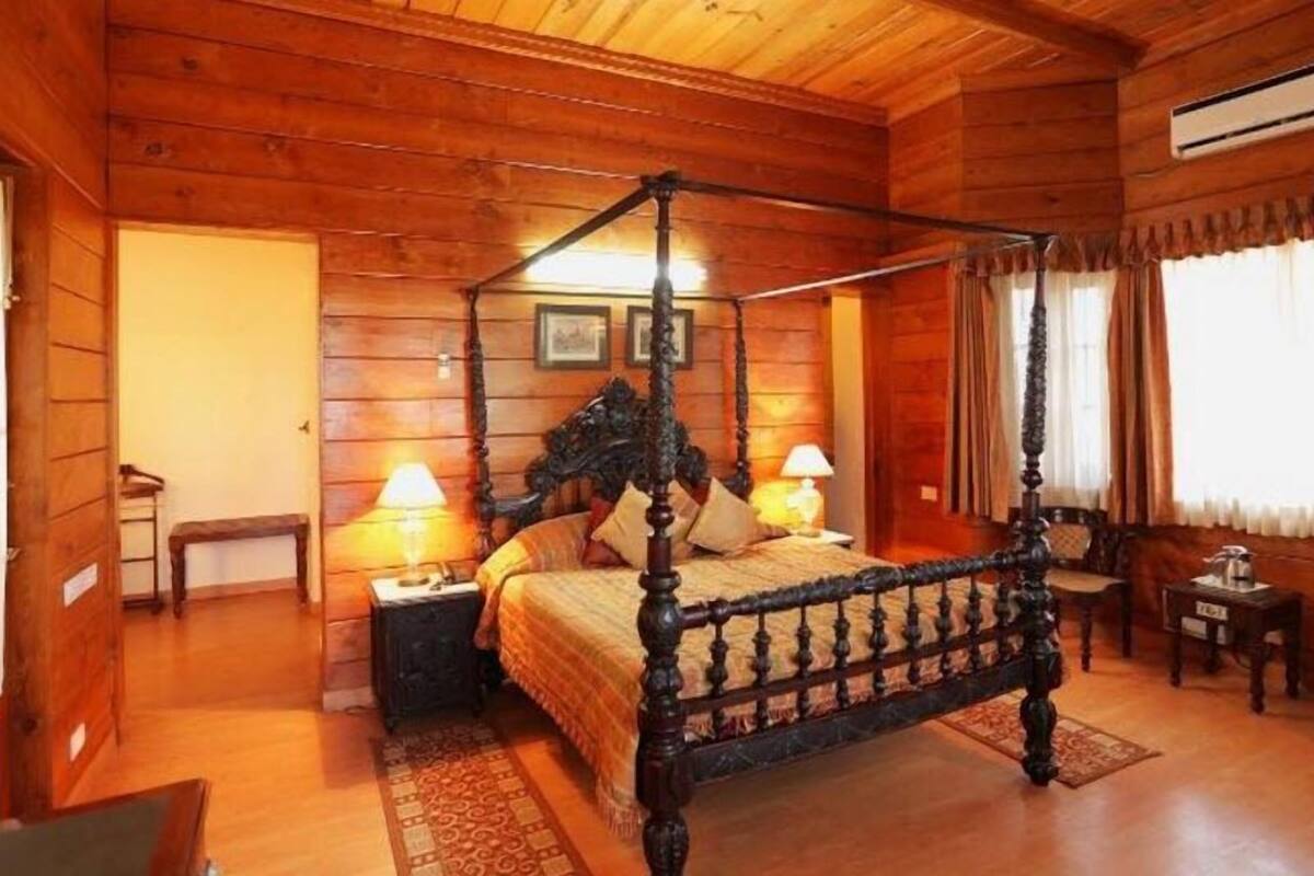 A wooden four-poster bed with two bedside tables, a bench, and a small table with a lamp.