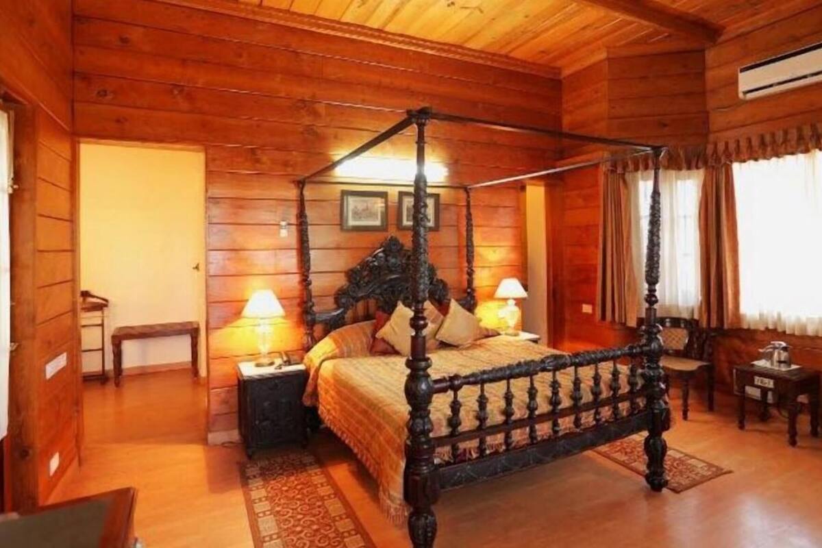 A four-poster bed with a wooden headboard, two bedside tables with lamps, a bench, and a small table with a lamp.
