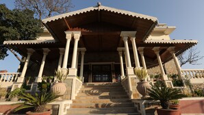 A building with a central entrance, flanked by columns, and a staircase leading up to it. - WelcomHeritage Windsor Lodge (Ranikhet)