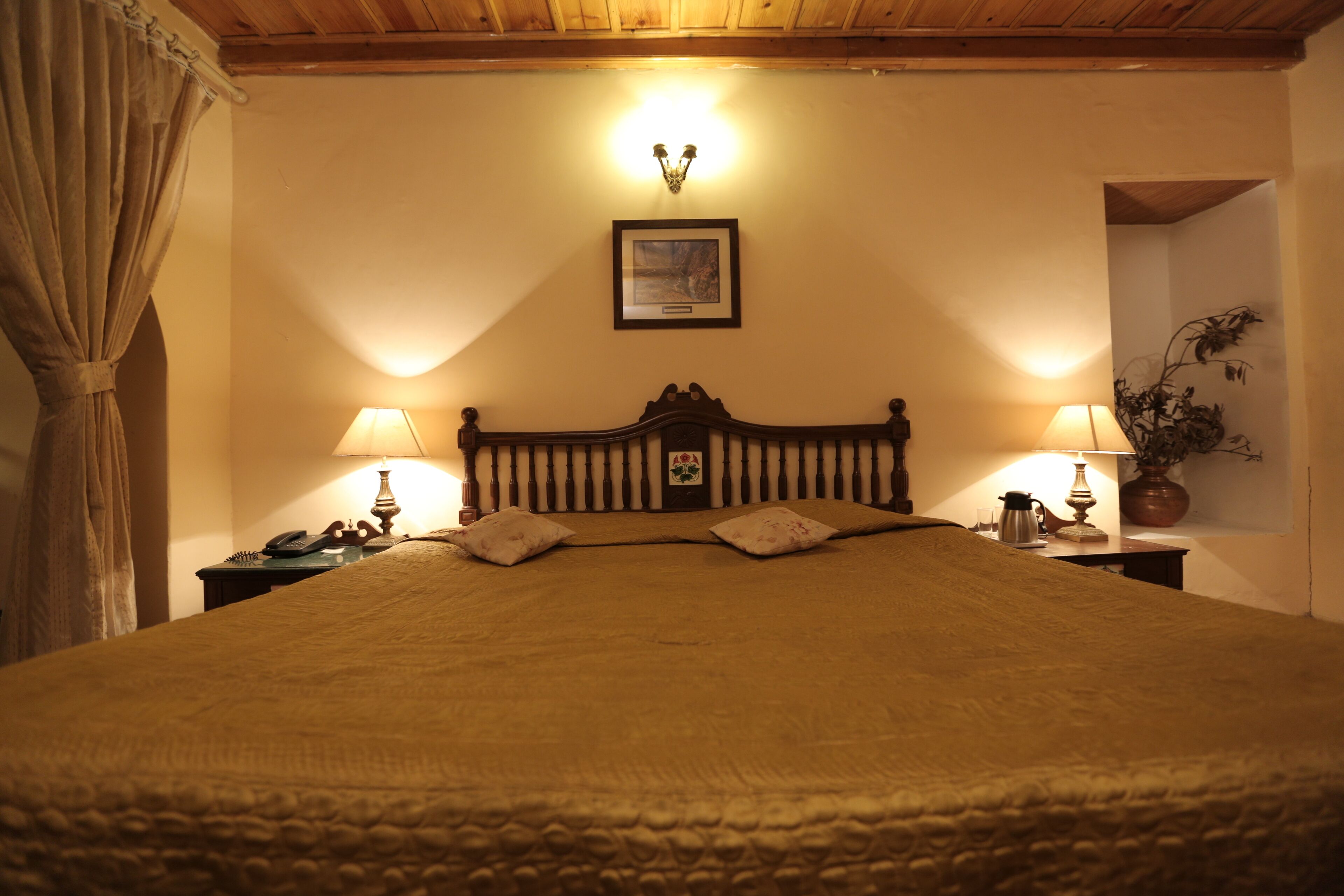 A neatly made bed with a wooden headboard, two bedside lamps, and a framed picture on the wall.