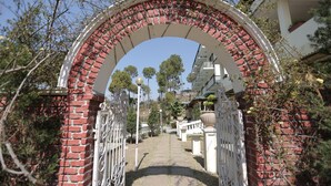 A brick archway with a metal gate leading to a pathway. - WelcomHeritage Windsor Lodge (Ranikhet)