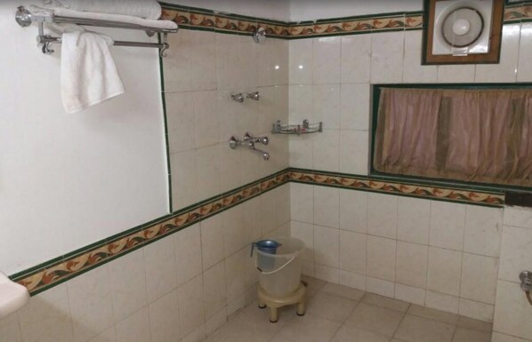 A small bathroom with white tiled walls, a shower, a toilet, and a towel rack.