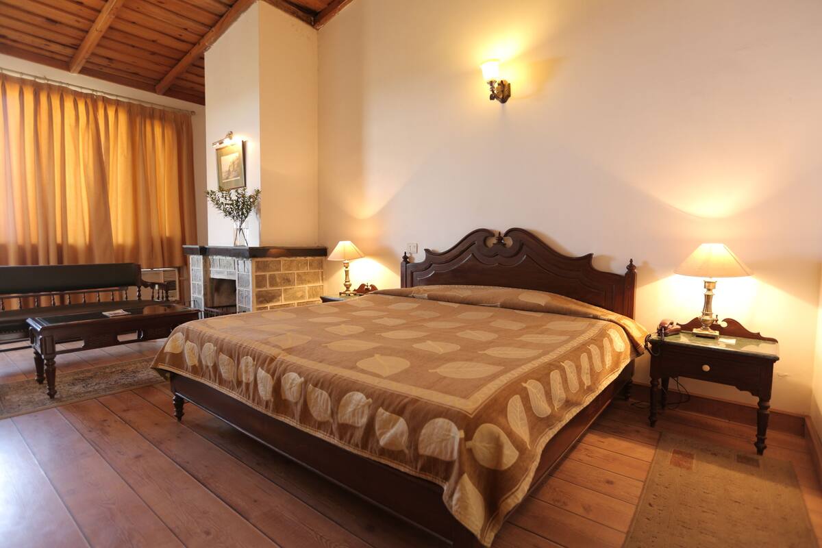 A bedroom with a large bed, wooden flooring, a fireplace, and two bedside lamps.
