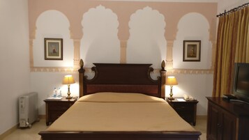A hotel room with a large bed, two bedside tables with lamps, a radiator, and a television on a cabinet.