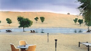 Un paysage désertique avec une piscine, des chaises longues et un petit pavillon.