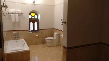 A bathroom with a bathtub, toilet, and a window with stained glass.