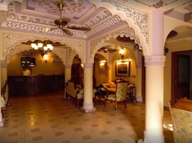 Un vestíbulo con arcos decorativos, una recepción y un área de estar con sillas y mesas.