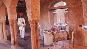 A historic building with arched stone columns, a central table with a decorative cloth, and a person in traditional attire walking through the space.