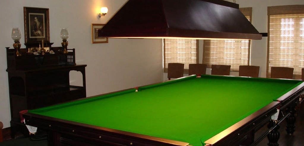 A pool table in a room with a dark ceiling vent, a framed picture on the wall, and a window with blinds.
