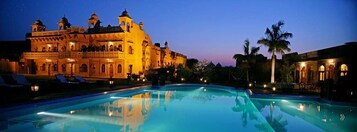Un edificio grande e iluminado con una piscina al frente.