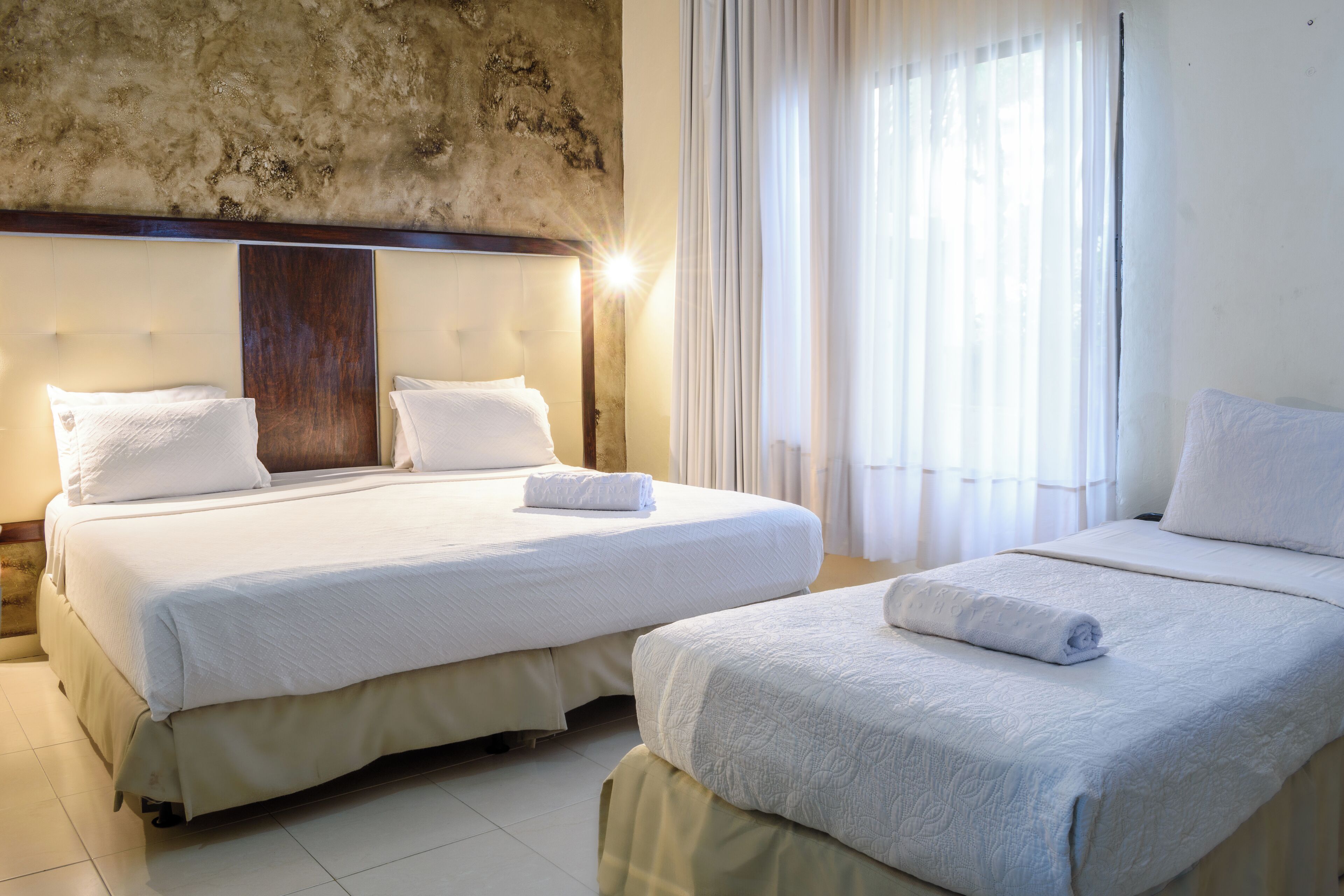 A hotel room with two beds, a stone wall, and a large window with curtains.