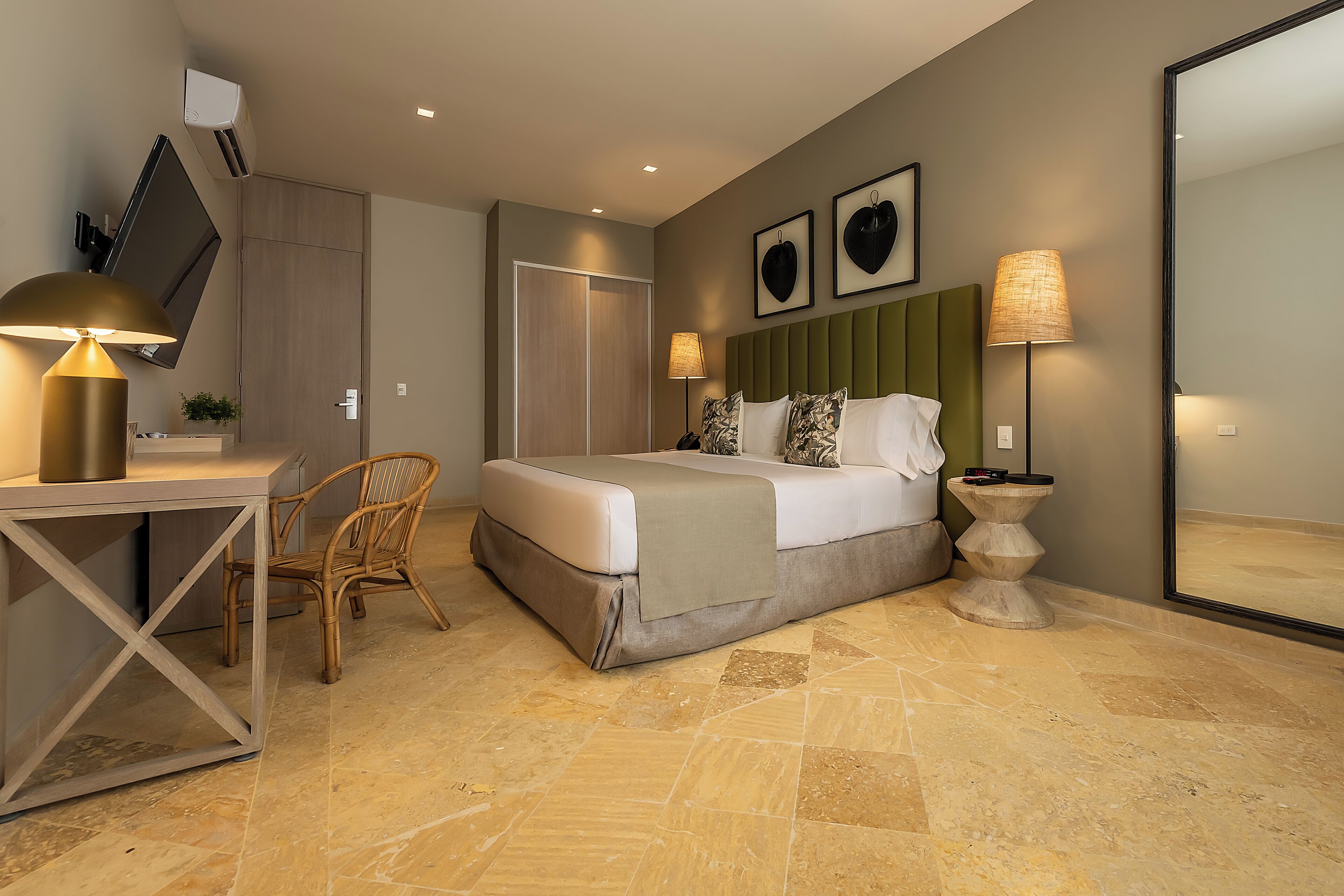 Quarto de hotel moderno com cama, escrivaninha, cadeira, abajur e um espelho grande.