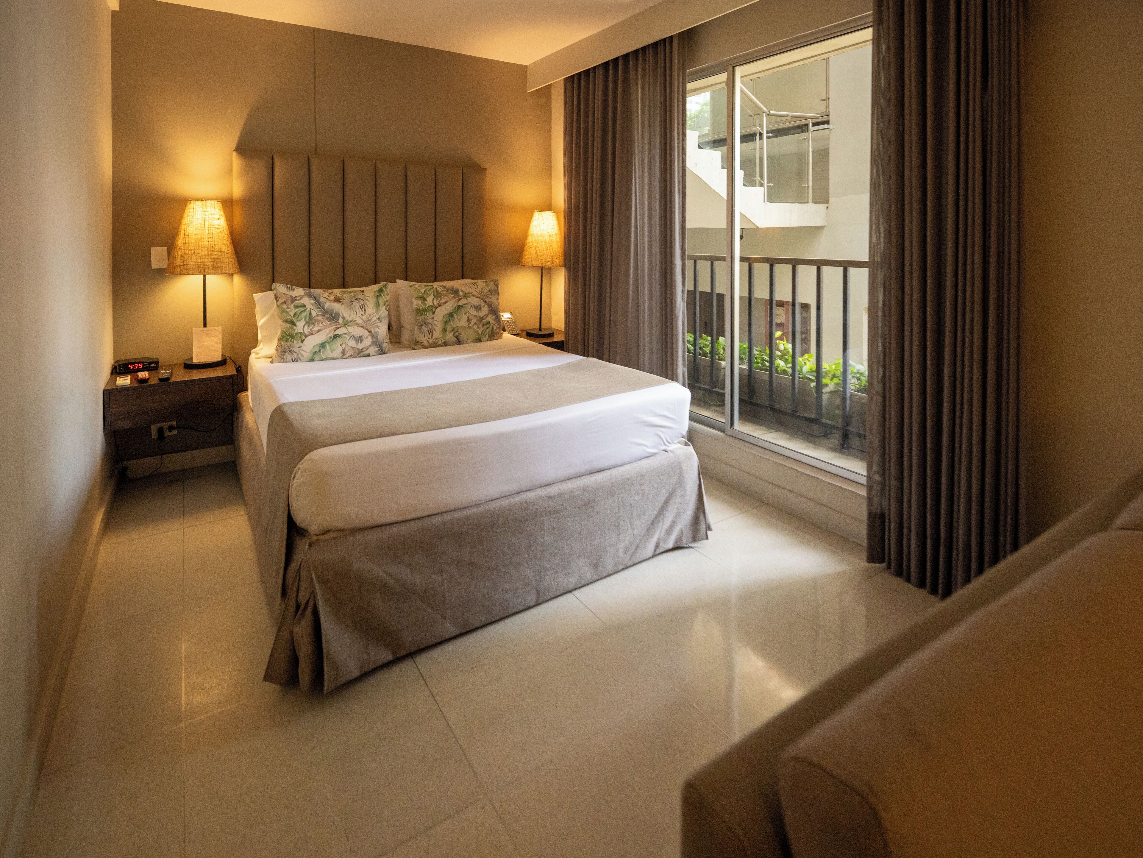 A hotel room with a large bed, two bedside lamps, a nightstand, and a view of the outside balcony.