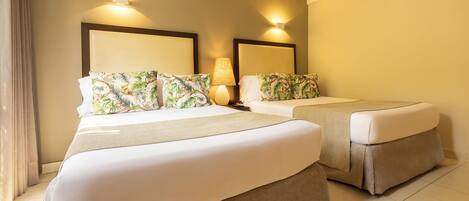 A hotel room with two beds, each with a headboard and matching pillows. There is a lamp on one side of the room.