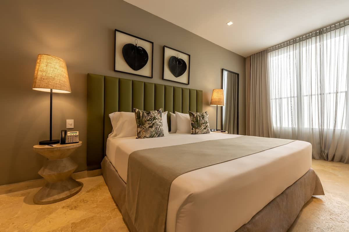 A hotel room with a large bed, two wall-mounted heart-shaped decorations, a bedside lamp, and a window with curtains.