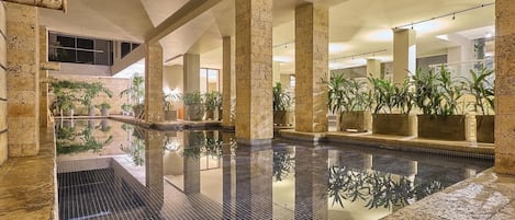 An indoor swimming pool with stone columns, potted plants, and a tiled floor.