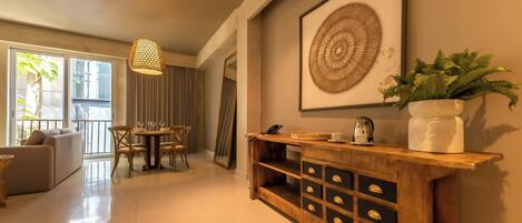 A modern living room with a sofa, dining table, and chairs, a wooden console with drawers, a large framed artwork, and a potted plant.