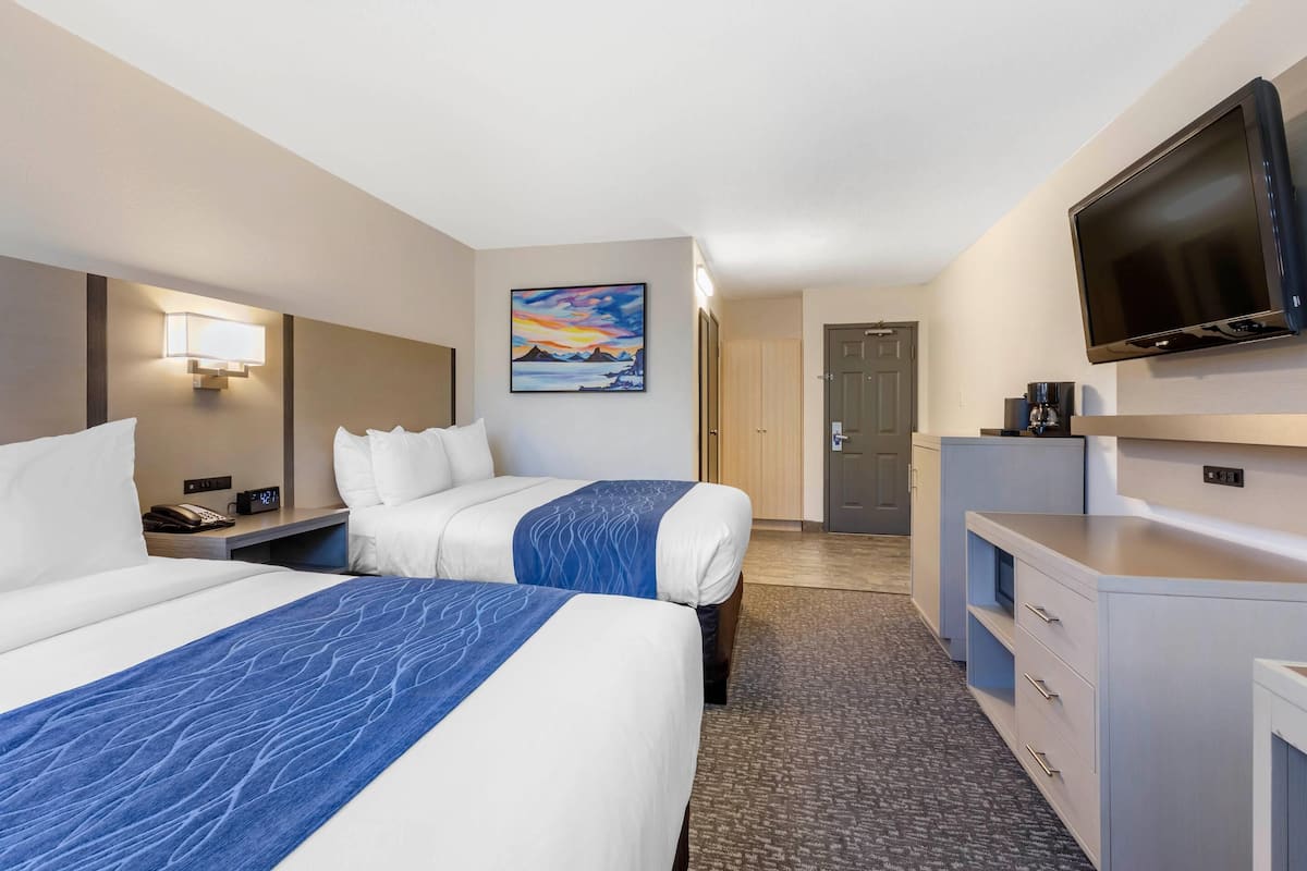 A hotel room with two beds, a TV, a desk, and a painting on the wall.