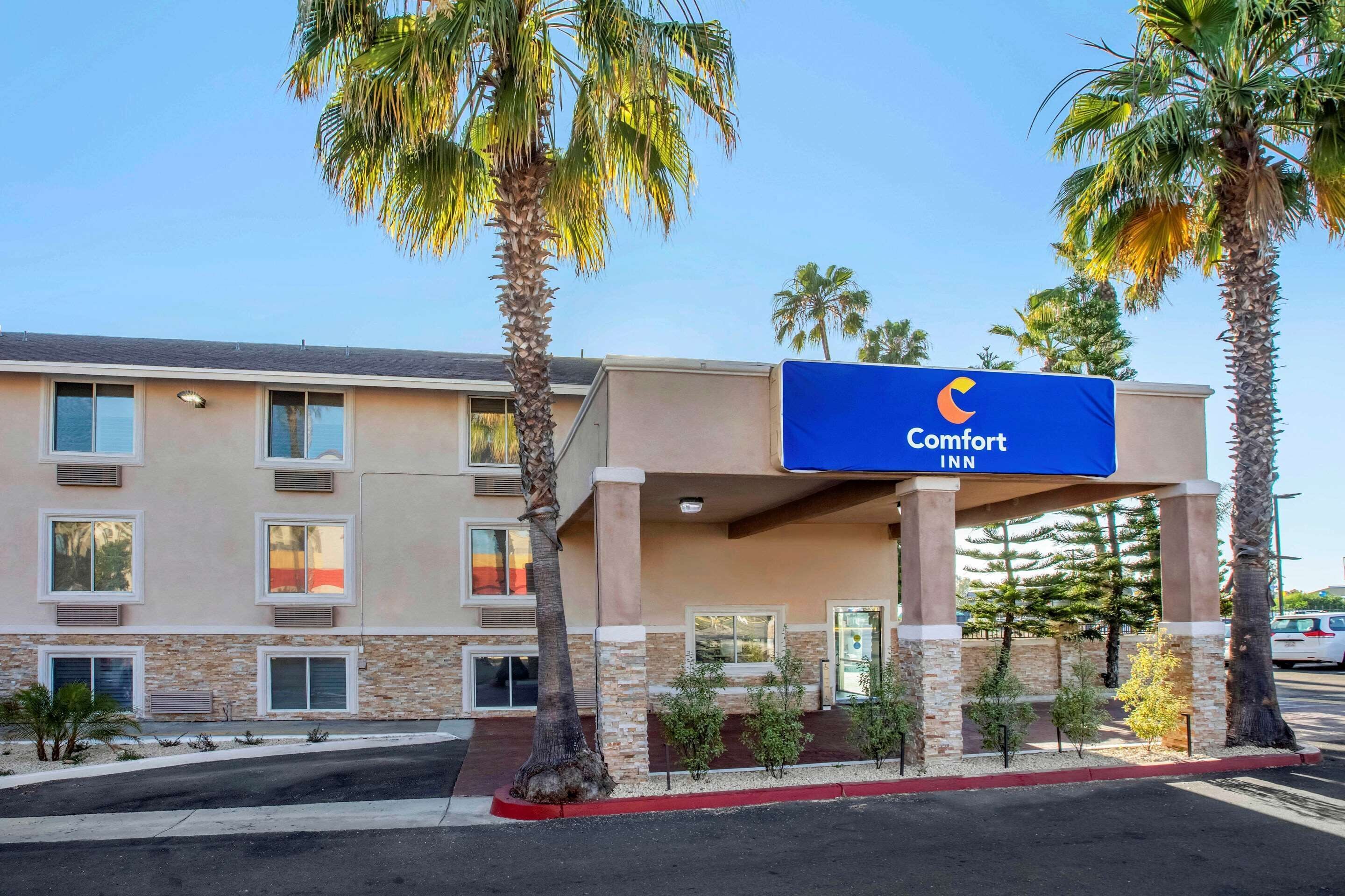Un hotel Comfort Inn con fachada moderna, varias ventanas y palmeras frente a él.