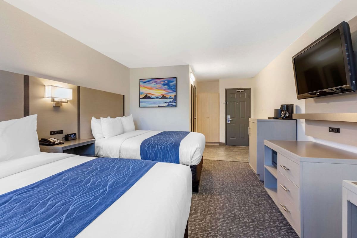 A hotel room with two beds, a TV, a desk, and a painting on the wall.