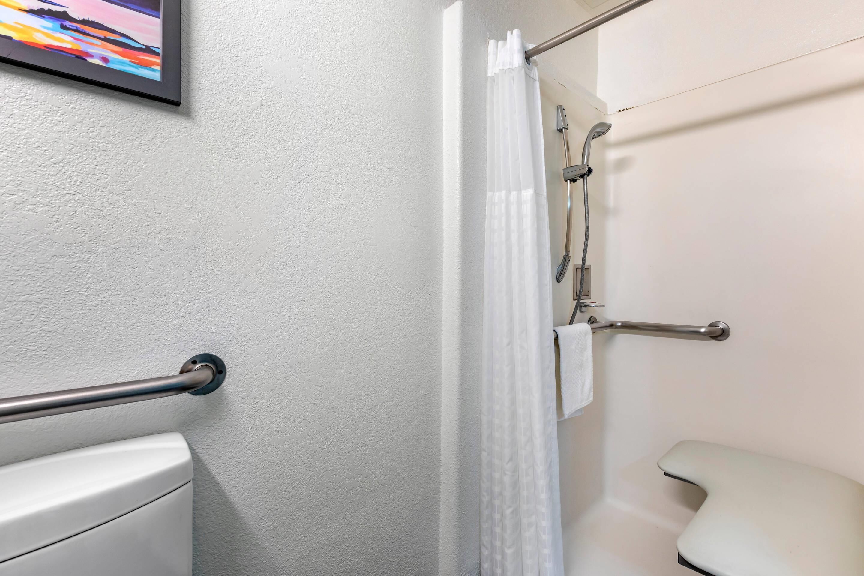 Un baño con inodoro blanco, ducha con puerta de cristal y barra de apoyo.