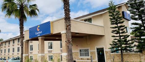 A Comfort Inn hotel with a stone facade, palm trees, and a clear blue sky.