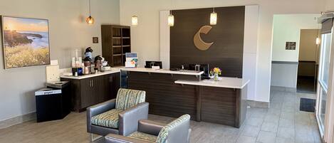A modern reception area with a desk, two cushioned chairs, a large wall-mounted clock, and a framed picture.