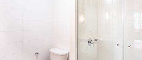 Bagno con servizi igienici, cabina doccia in vetro e pareti rivestite di piastrelle bianche.