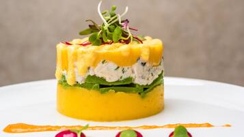 A layered dish with a yellow base, green middle layer, and white top layer, garnished with microgreens and radish slices.