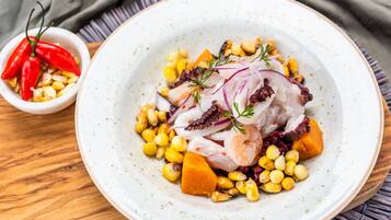 Plato de comida con pulpo, maíz y cebollas rojas, acompañado de un recipiente pequeño con chiles rojos.