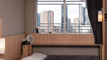 Habitación de hotel con cama, mesita de noche con lámpara, teléfono y ventana con vista a edificios.