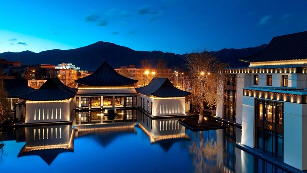 A traditional building with a reflective pool, surrounded by mountains and lit by ambient lighting.