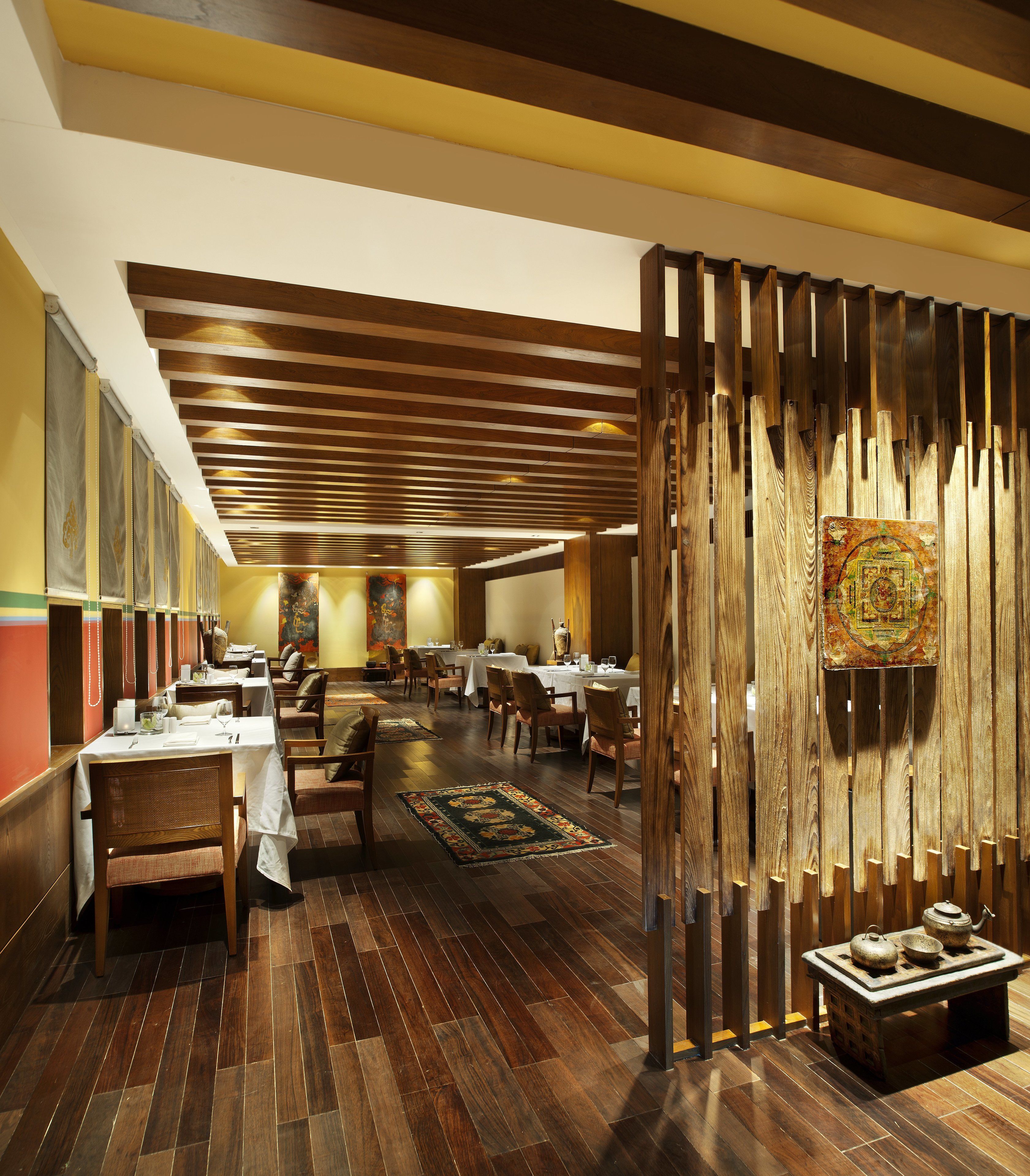 Restaurante com soalho de madeira, mesas, cadeiras e um divisório decorativo em madeira.