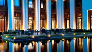 A hotel exterior with a pool, outdoor seating, and illuminated windows.